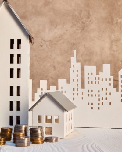 stock-photo-coins-houses-models-white-wooden-table-brown-textured-wall-paper